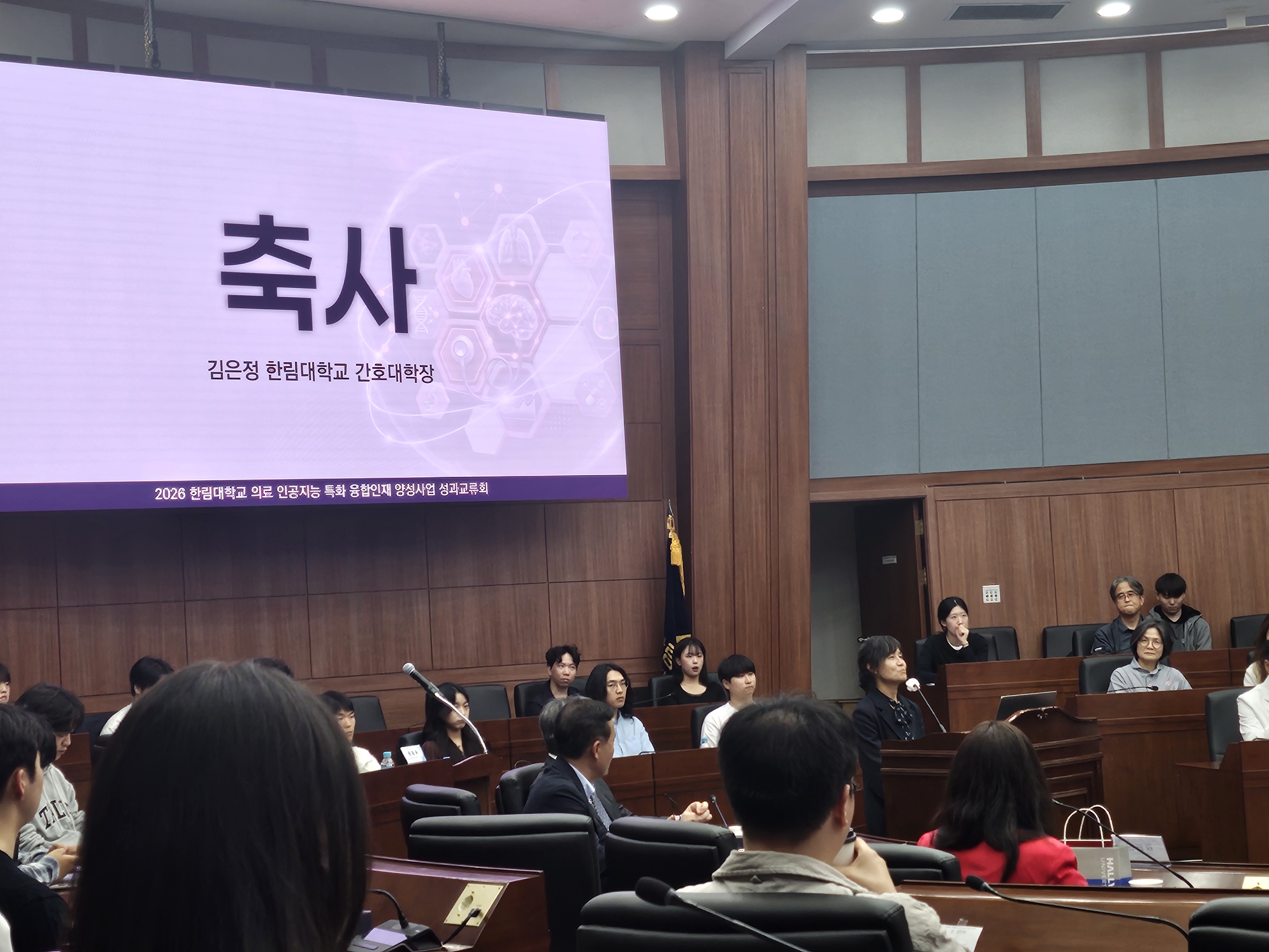 2026년 의료 인공지능 특화 융합인재 양성사업 성과교류회에서 한림대학교 간호대학장 김은정 교수가 원형 강의실 중앙 단상에서 축사를 낭독학고 있다.